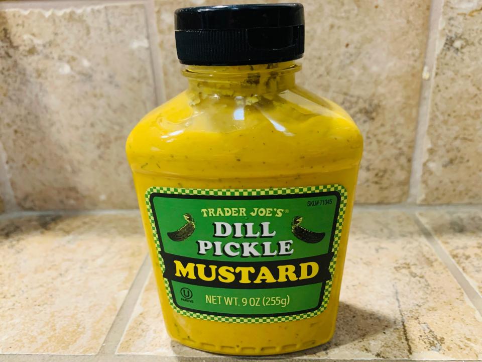 Trader Joe's dill-pickle mustard, which is bright yellow and in the original bottle, against a beige tile background