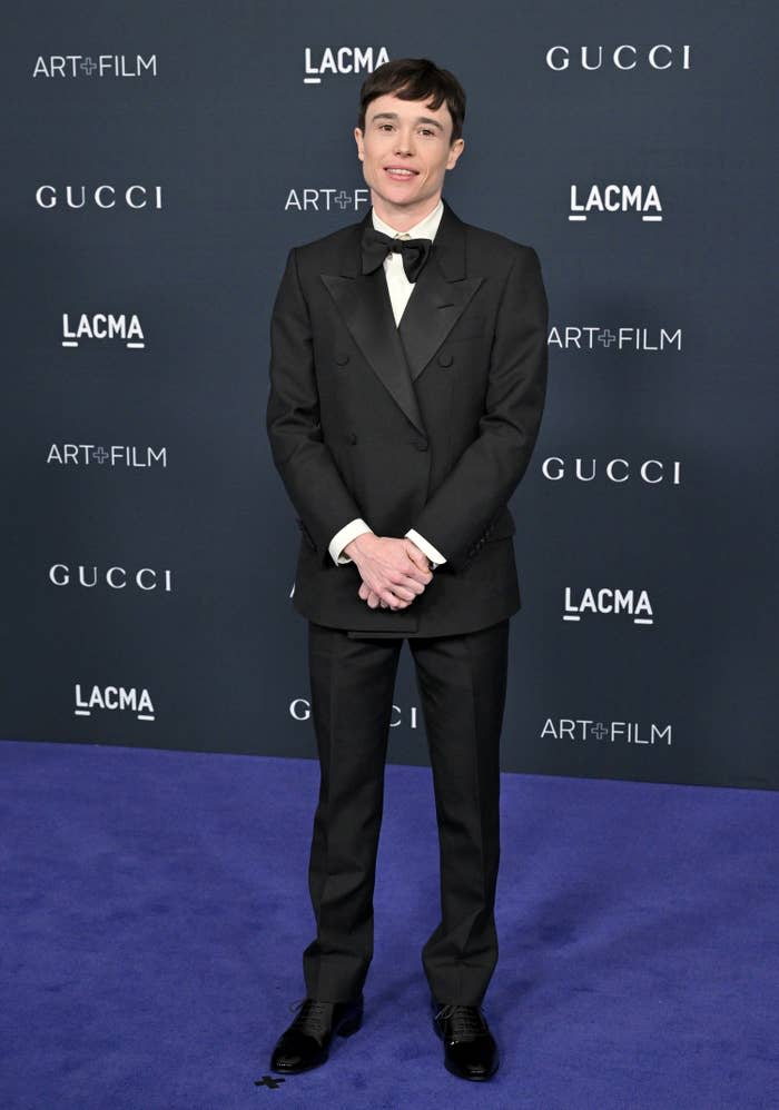 Elliot Page smiles on the red carpet of a formal event wearing a tux