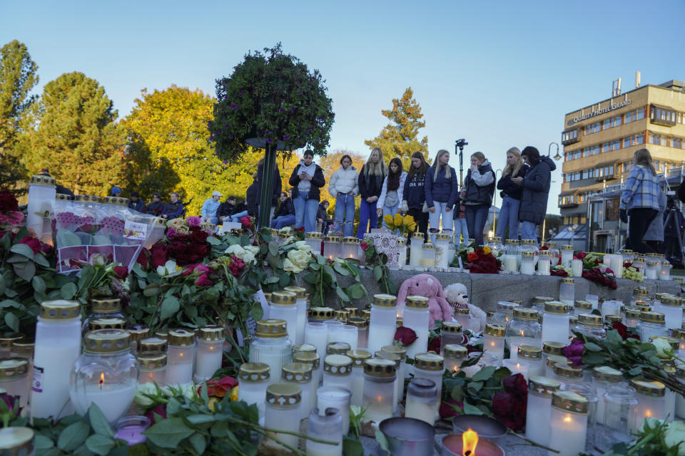 Young people look at the floral tributes and candles left for the victims of a bow and arrow attack, on Stortorvet in Kongsberg, Norway, Friday, Oct. 15, 2021. The suspect in a bow-and-arrow attack that killed five people and wounded three in a small Norwegian town is facing a custody hearing Friday. He won’t appear in court because he has has confessed to the killings and has agreed to being held in custody. (Terje Bendiksby/NTB via AP)