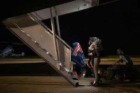FILE PHOTO: A child from Honduras, draped in a covering with an image of the American flag, walks ahead of his mother towards a plane deporting migrants back to Honduras from Mexico, at the Tapachula International Airport in Tapachula, Mexico October 31, 2018. REUTERS/Carlos Garcia Rawlins/File Photo