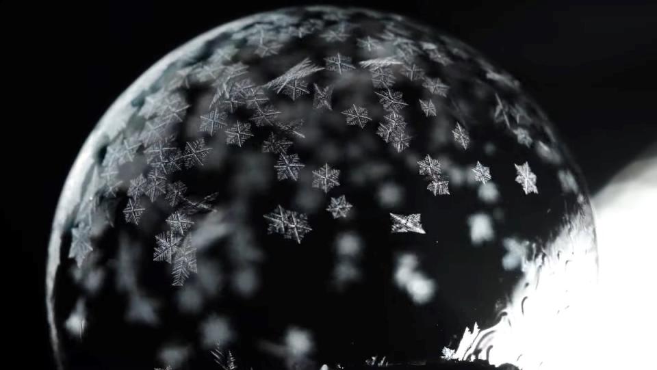 A soap bubble begins to freeze with tiny snowflakes forming