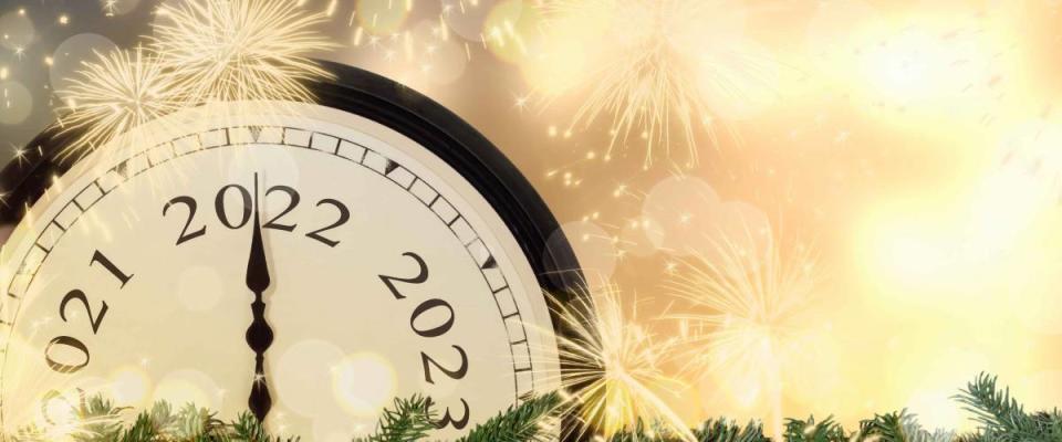 New Year's Eve 2022 concept. Clock hands on year number 2022. Gold magic background with fireworks and blurred lights.