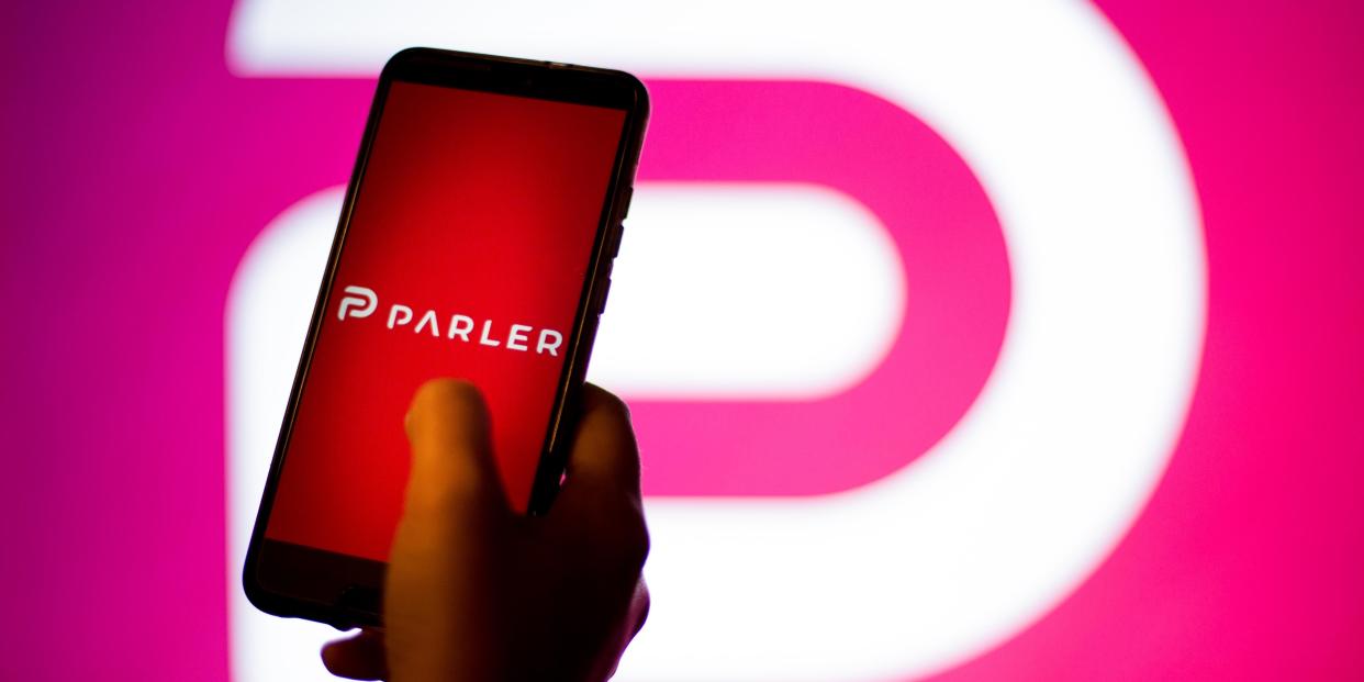 A hand holding a phone with Parler logo on the screen and background.
