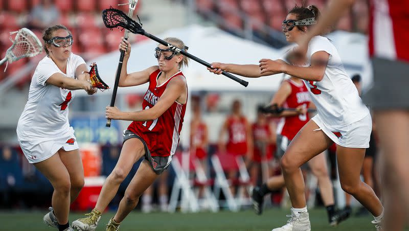 Mountain Ridge’s Tessa Mortensen, center, crosses in the middle and is met with the Skyridge defense of Brooklyn Gibson, left, and Alex Vaughn during the Utah 6A Girls Lacrosse State Championship game between Mountain Ridge and Skyridge at Zions Bank Stadium in Herriman, Utah on Saturday, April 23, 2022.