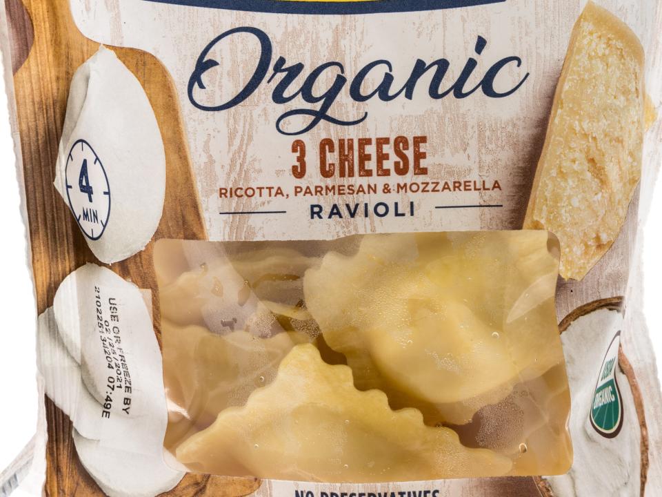 A bag of pre-packaged ravioli with a picture of an old man on front with "Giovanni Rana" and "Organic 3 Cheese Ravioli" text. Bag has a window in which the customer can see the pieces of piece inside