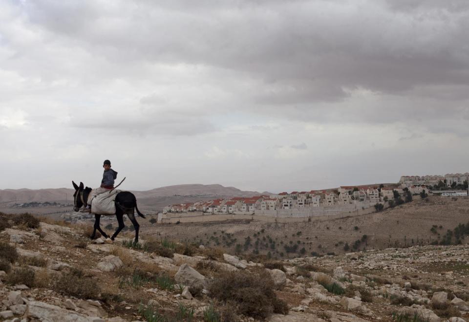 FILE - In this Wednesday, Dec. 5, 2012 file photo, a Palestinian boy rides a donkey in the E-1 area near the West bank settlement of Maaleh Adumim, background, on the eastern outskirts of Jerusalem. Israel's prime minister is moving ahead with a contentious law that would legalize dozens of settlement outposts in the West Bank, despite claims by experts that the bill itself is illegal a warning from the White House that settlement construction "may not be helpful." (AP Photo/Sebastian Scheiner, File)