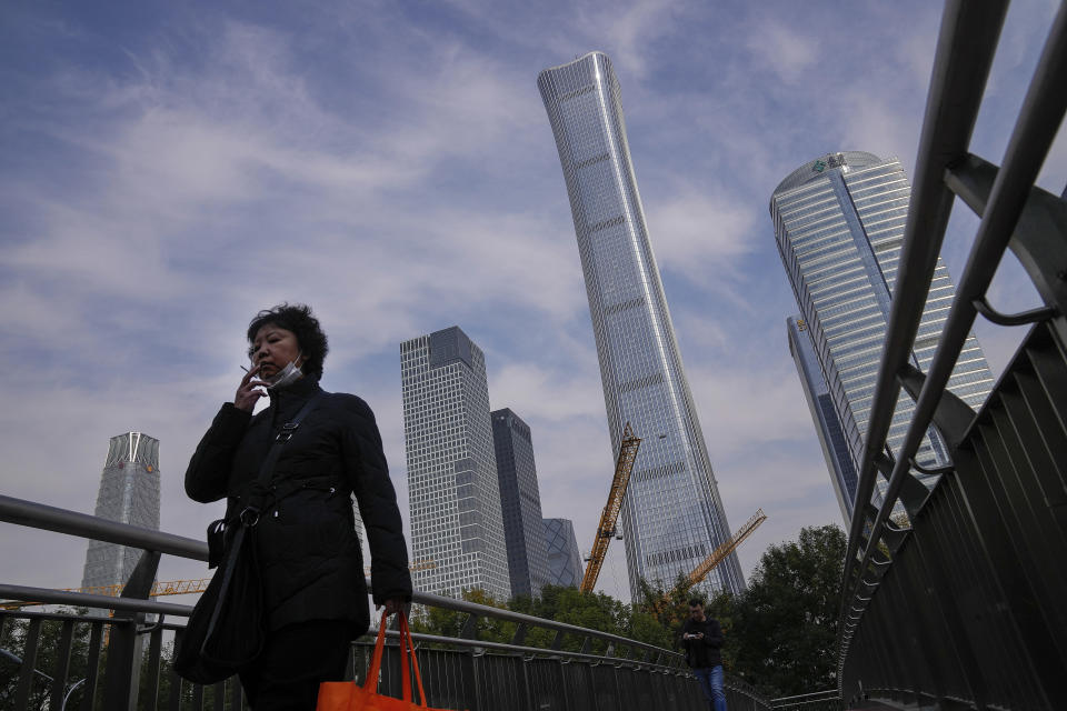 A woman wearing a face mask smokes as she walks by construction cranes stand near the skyscrapers at the Central Business District in Beijing, Monday, Oct. 18, 2021. China's economic growth sank in the latest quarter as a slowdown in construction and curbs on energy use weighed on its recovery from the coronavirus pandemic. (AP Photo/Andy Wong)