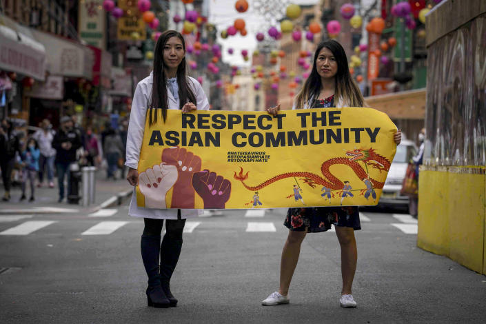 Dr. Michelle Lee, left, a radiology resident, and Ida Chen, right, a physician assistant student, unfold a banner Lee created to display at rallies protesting anti-Asian hate, Saturday April 24, 2021, in New York's Chinatown. Lee, who is Korean-born, and Chen, who is American-born Chinese, join medical professionals of Asian and Pacific Island descent who feel the anguish of being racially targeted because of the virus while toiling to keep people from dying of it. (AP Photo/Bebeto Matthews)