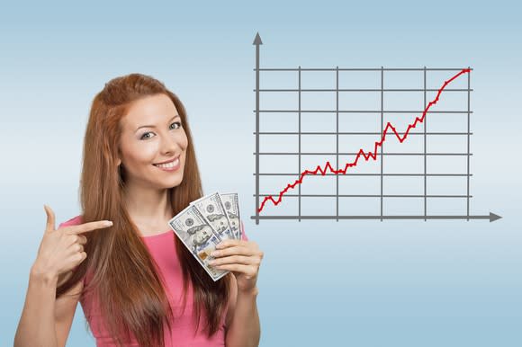 A woman holding a fanned stack of cash next to a rising stock chart.