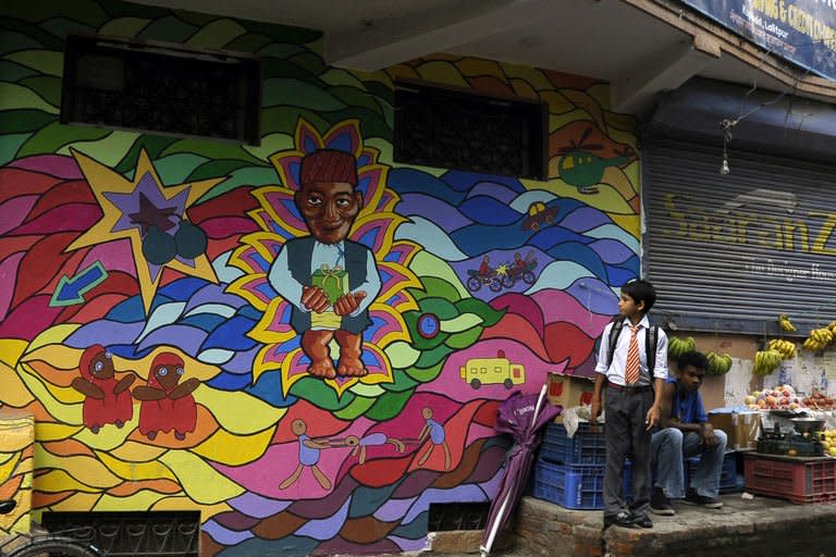 A Nepalese schoolboy looks at a mural while standing beside a vegetable vendor in Kathmandu on August 20, 2013. Some 60 artists have been involved in the project called "Kolor Kathmandu" which began in January and will culminate on Thursday with the launch of a book of photographs on the murals