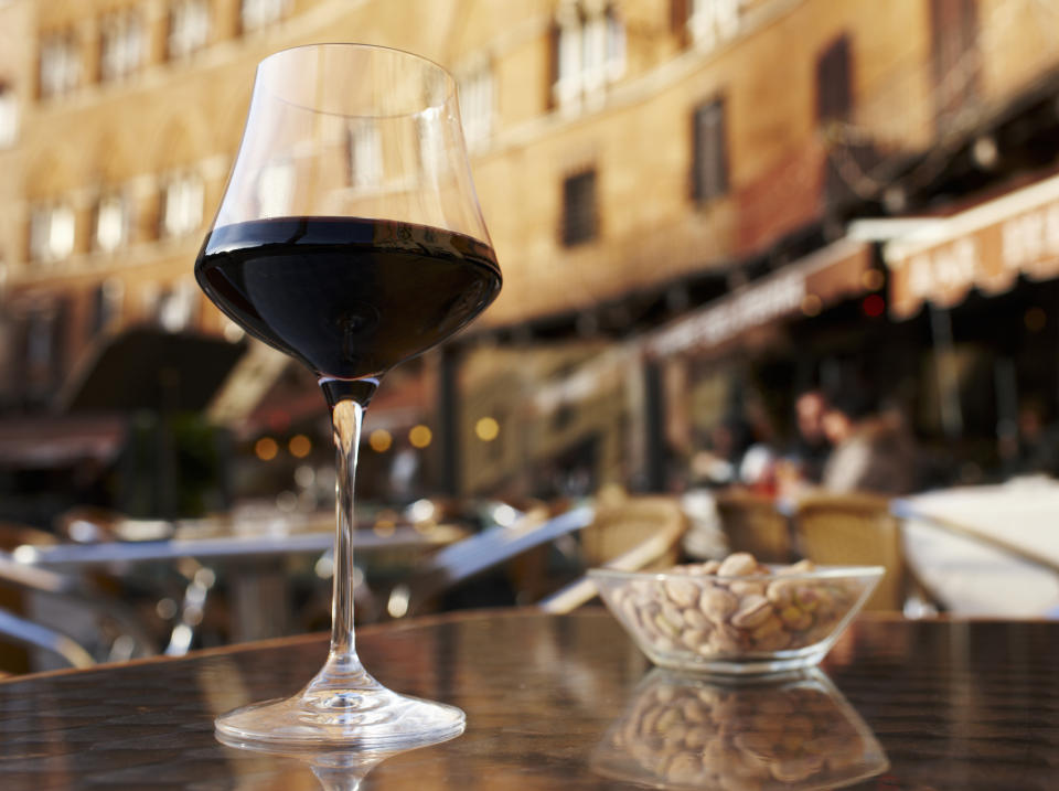 Glass of red wine on a table at an outdoor cafe with blurred background of buildings and people