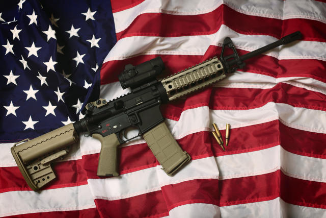 An AR-15 rifle with bullets on an American flag. 