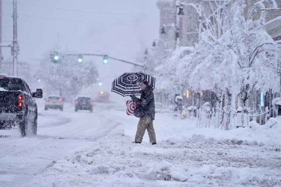 A passer-by uses an umbrella while crossing a snow-covered street, Tuesday, March 14, 2023, in Pittsfield, Mass. The New England states and parts of New York are bracing for a winter storm due to last into Wednesday. (Ben Garver/The Berkshire Eagle via AP)