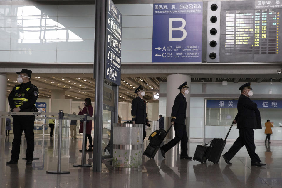 FILE - In this March 12, 2020, file photo, air crew members walk past the international arrival exit at the Capital International Airport terminal 3 in Beijing. President Donald Trump has repeatedly credited his February ban on travelers from mainland China as his signature move against the advance of the coronavirus pandemic -- a “strong wall” that allowed only U.S. citizens inside, he boasted in May. But Trump’s wall was more like a sieve. Exempted were thousands of residents of the Chinese territories of Hong Kong and Macau. (AP Photo/Ng Han Guan, File)