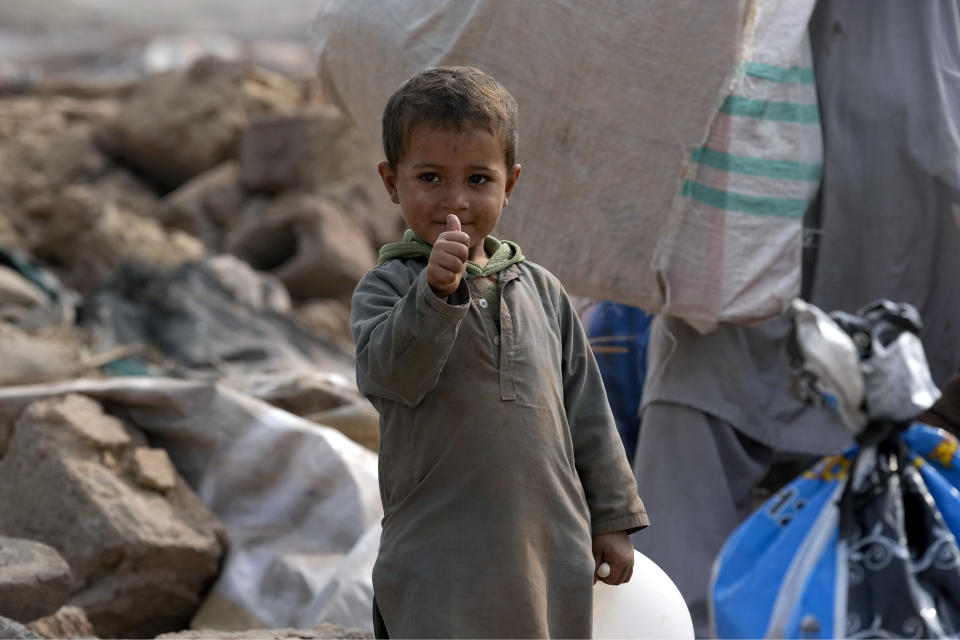 An Afghan boy gestures as he stands beside his family's belongings retrieved from their damage mud homes demolished by authorities during a crackdown against an illegal settlement and immigrants, on the outskirts of Islamabad, Pakistan, Wednesday, Nov. 1, 2023. (AP Photo/Anjum Naveed)