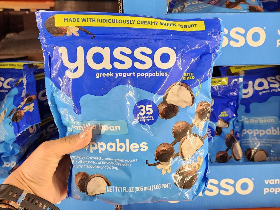 A hand holds a blue plastic bag of Yasso Greek yogurt poppables with a picture of chocolate-covered balls of Greek yogurt