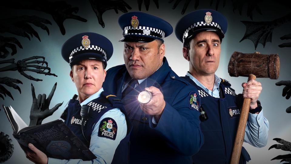 Three police officers look at the camera while black demon hands reach out for them in a publicity shot for Wellington Paranormal