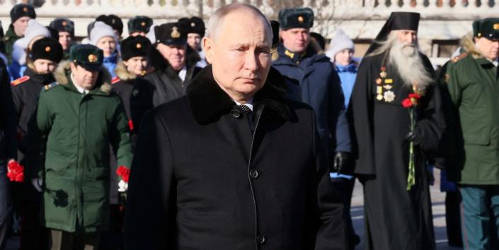 Russian President Vladimir Putin wears a black coat, walks in front of military officials outdoors, February 23, 2023.