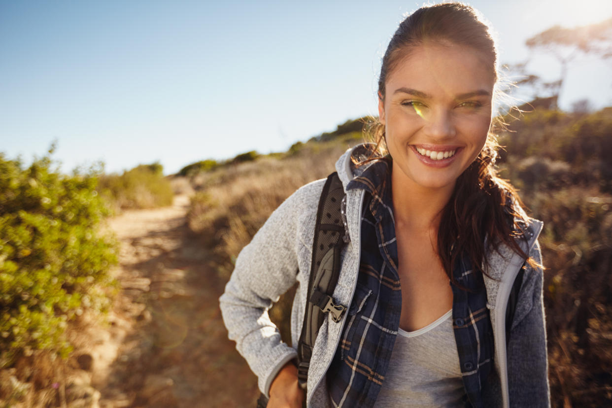 Hiker hiking in nature. Young woman smiling during hike. Caucasian female model outdoors on hike looking at camera. Enjoying summer vacation in countryside.