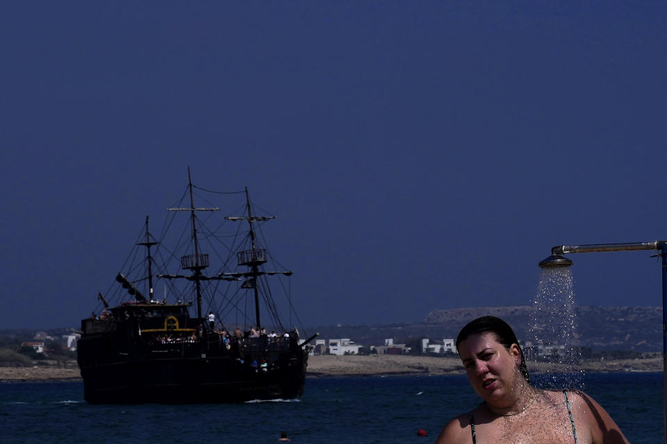 A tourist takes a shower as a tourist cruise ship, copy of pirates ship, passes on the sea at Limanaki beach in southern coastal resort of Ayia Napa in southeast Mediterranean island of Cyprus, Sunday, June 5, 2022. Hundreds of Russian and Ukrainian Orthodox faithful visiting Cyprus would stream daily past the icon of the Virgin Mary at Kykkos Monastery to venerate the relic that tradition dictates was fashioned by Luke the Evangelist and blessed by the Virgin herself. But a European Union ban on flights to and from Russia as a result of Russia's invasion of Ukraine has meant a loss of 800,000 vacationers - a fifth of all tourists to Cyprus in record-setting 2019. (AP Photo/Petros Karadjias)