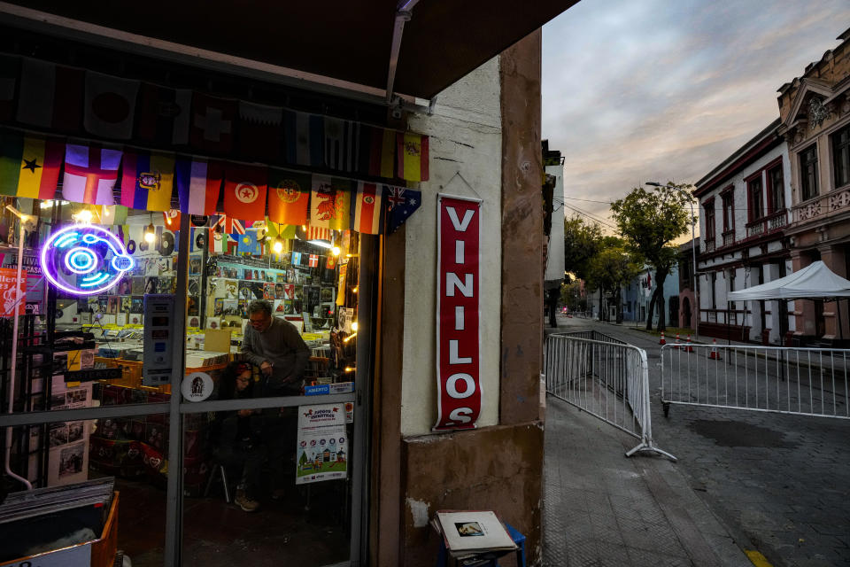 Trabajadores de una tienda conversa en un local de vinilos en el barrio de Yungay en Santiago, Chile, el 6 de junio de 2024. Un albergue para personas sin hogar está ubicado en el mismo bloque, y el domicilio del presidente chileno, Gabriel Boric, está cruzando la calle, rodeado de vallas metálicas que bloquean el paso de vehículos. (AP Foto/Esteban Félix)