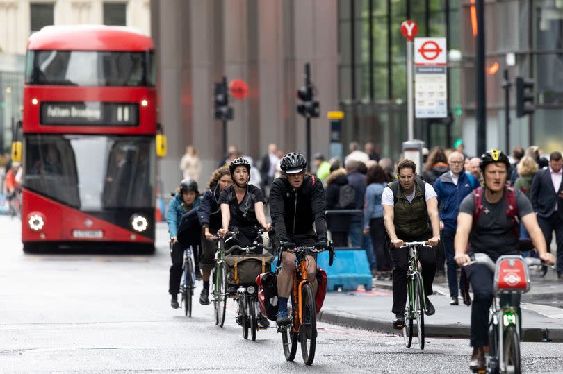 Cyclists pass commuters waiting at a London bus stop