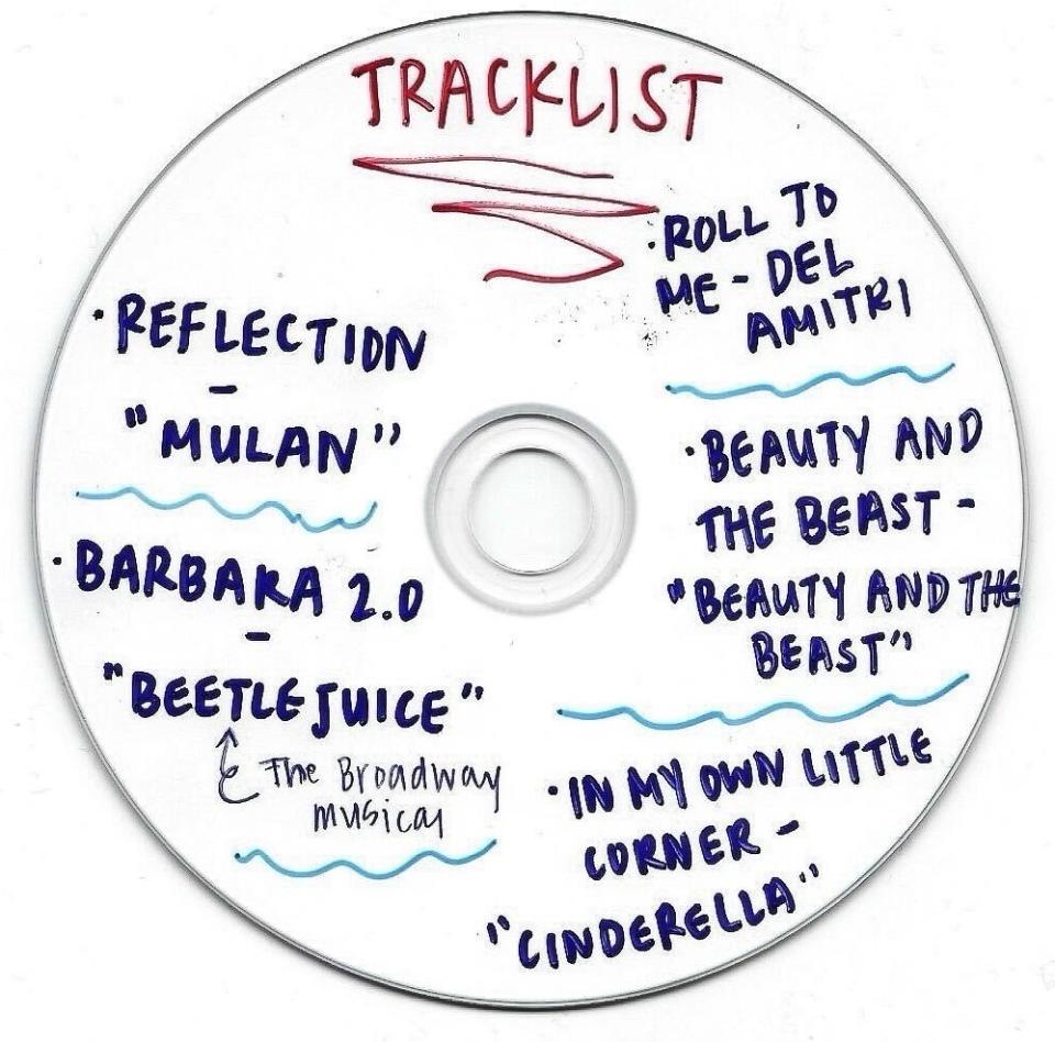 A white CD with a handwritten tracklist including songs: Reflection (Mulan), Barbara 2.0, Beetlejuice (The Broadway Musical), Roll to Me (Del Amitri), Beauty and the Beast, In My Own Little Corner (Cinderella)