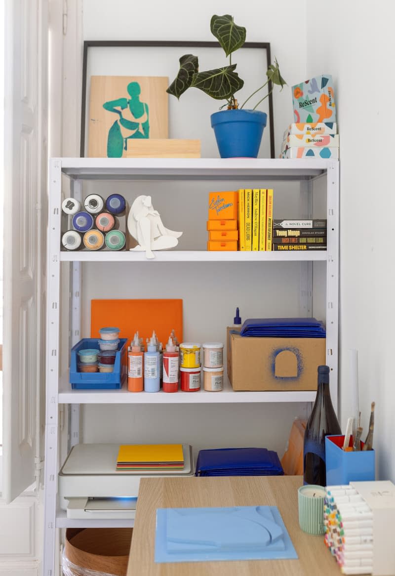 Art supplies on a white storage rack with a studio space.