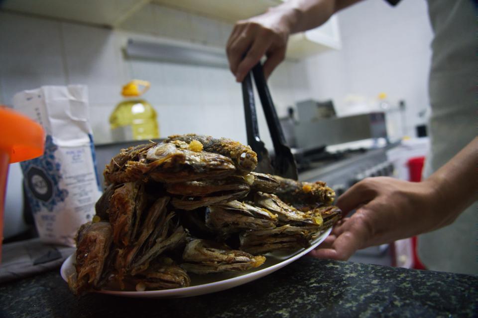 In this Wednesday, June 3, 2020 photo, Gary Dela Pena of Laguna, Philippines, puts fried mackerel on a plate to help Feby Cachero Baguisa Dela Pena feed those who need it in Dubai, United Arab Emirates. Dela Pena, a mother of three, is unemployed, but when she saw people lining up for free meals one night outside her building two weeks ago she decided to use whatever money her family had to help out the countless numbers of Filipinos and others who've lost jobs amid the coronavirus. (AP Photo/Jon Gambrell)