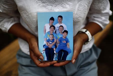 Cheng Liping, whose husband Ju was onboard Malaysia Airlines Flight MH370 which disappeared on March 8, 2014 shows a family photo featuring her missing husband (top, R) at a park near her house where she and her husband used to visit, during an interview with Reuters in Beijing July 24, 2014. REUTERS/Kim Kyung-Hoon/Files