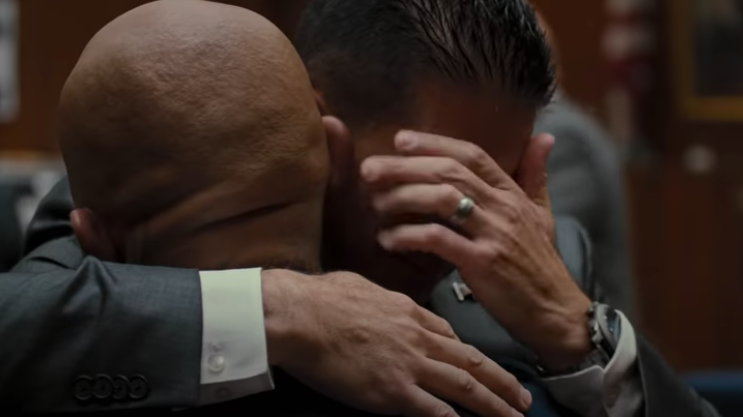 A man holds another man, who's crying, in a courtroom