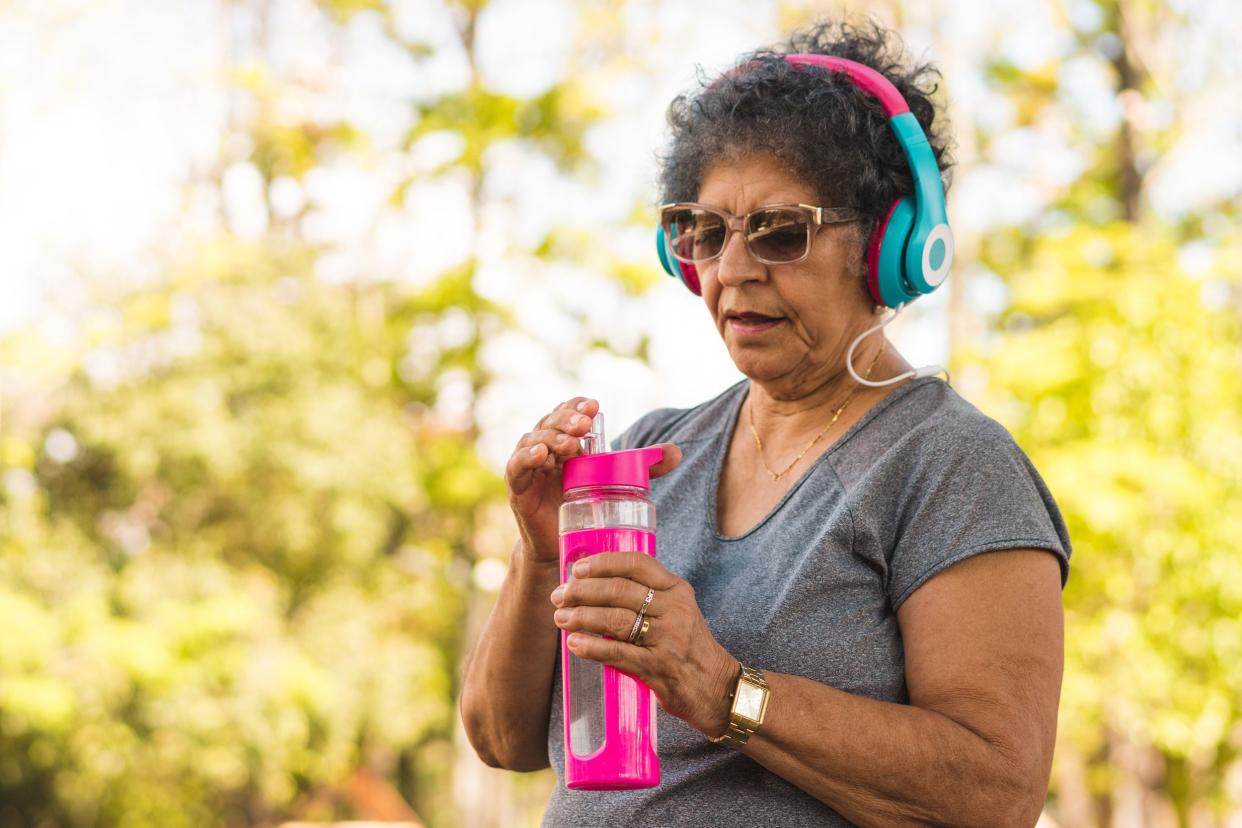 heated senior woman in park with exercise gear, about to drink water