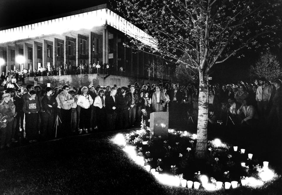 A crowd gathers on the edge of the Prentice Hall parking lot during the annual May 4 candlelight vigil observance at Kent State on May 3, 1982. The candles surround the small memorial at the edge of the parking lot. Taylor Hall is in the background.