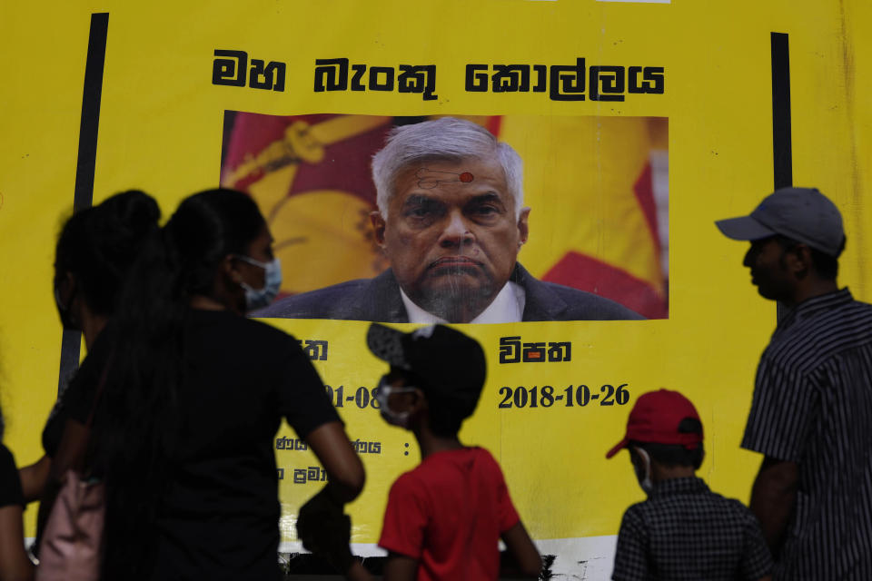 People watch propaganda materials displayed against prime minister Ranil Wickremesinghe outside president Gotabaya Rajapaksa's office three days after it was stormed by anti government protesters in Colombo, Sri Lanka, Tuesday, July 12, 2022. (AP Photo/Eranga Jayawardena)