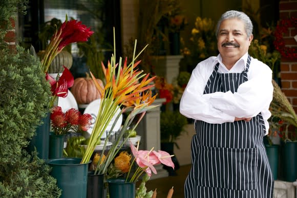 Smiling older man in apron outside a flower shop.