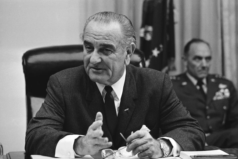 President Lyndon Johnson, sitting at his desk in a suit, tie and white shirt.