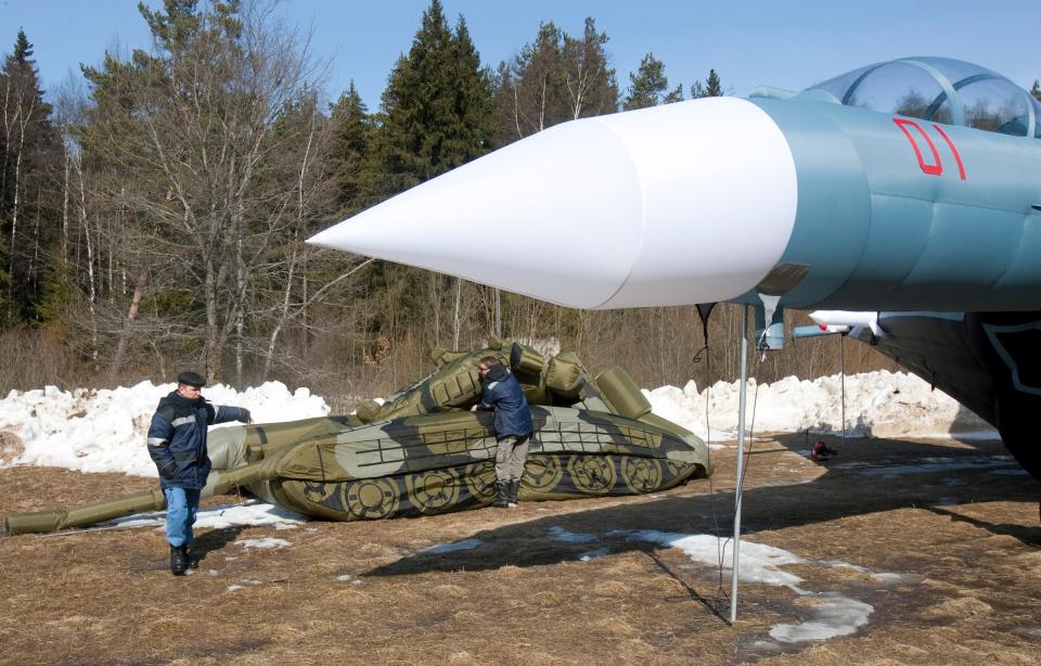 A worker sets up an inflatable tank next to a mostly inflated jet plane.