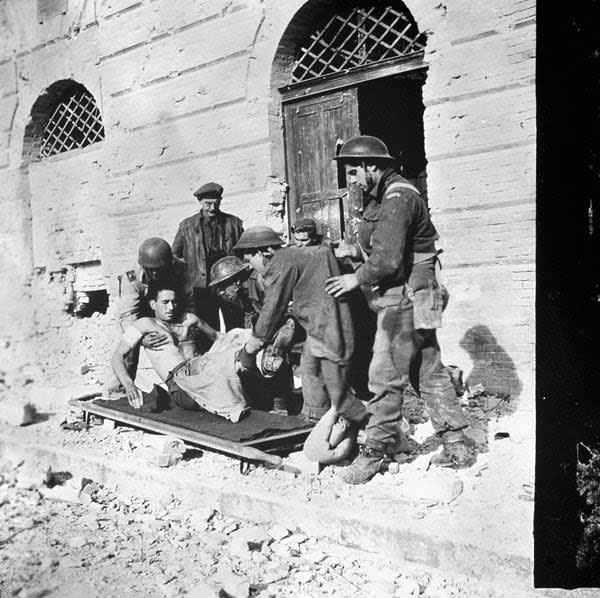 First-aid personnel of the Three Rivers Regiment placing Sgt. Johnny Marchand on a stretcher, in Ortona, Italy, on Dec. 21, 1943.