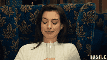 Anne Hathaway in "The Hustle" clinking her glass in the air