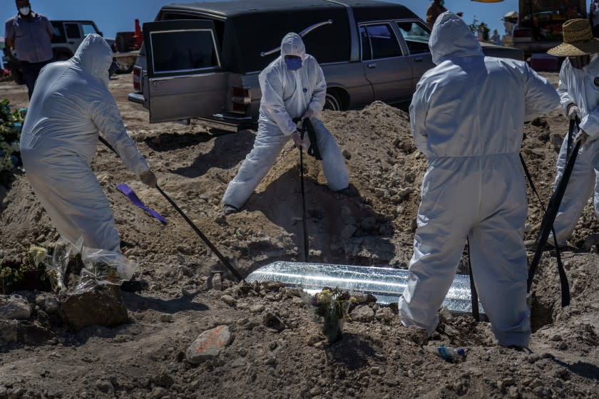 TIJUANA, BAJA CALIFORNIA -- SATURDAY, APRIL 25, 2020: Workers in protective suits lower a coffin carrying Laura Moreno Sanche, 49, who passed away due to COVID-19, towards a new crop of graves that are set aside for COVID-19 victims alongside other victims of violence and other diseases, at the municipal pantheon number 13 cemetery, in Tijuana, Mexico, on April 25, 2020. Not pictured, are her family members and friends watching the burial at a safe distance. (Marcus Yam / Los Angeles Times)