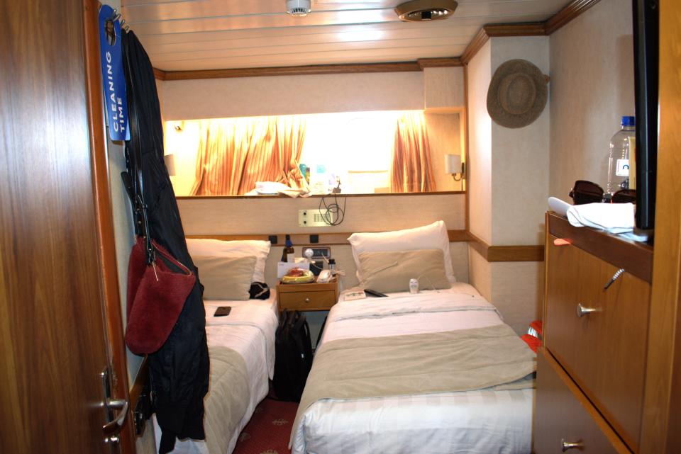 a hotel room with two beds with white and beige sheets in front of a window halfway up the wall