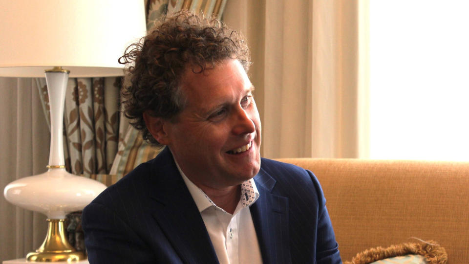 Close-up of a smiling man sitting on a couch in a hotel room.