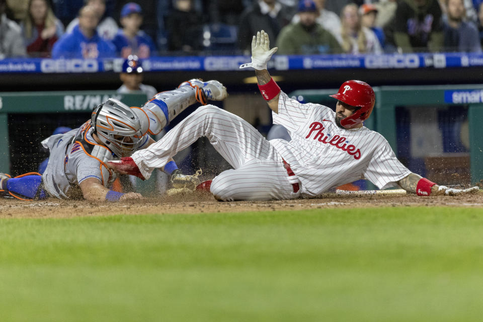Philadelphia Phillies' Nick Castellanos, right, scores on an RBI double by Rhys Hoskins before New York Mets catcher James McCann (33) can make the tag during the eighth inning of a baseball game, Monday, April 11, 2022, in Philadelphia. (AP Photo/Laurence Kesterson)