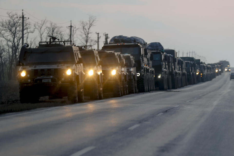 A convoy of Russian military vehicles with headlights on stretches into the distance.