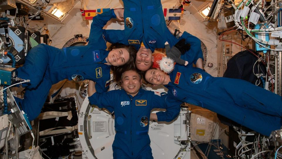  four astronauts with their heads together, floating in a circle on the space station 