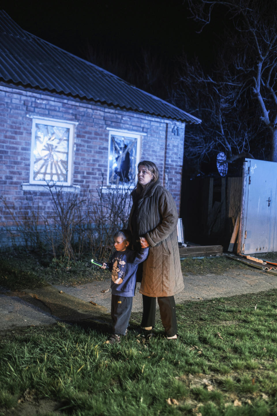 A woman with her child looks on fire outside of her house which was damaged after a Russian drone strike on residential neighborhood in Kharkiv, Ukraine, on Thursday, April. 4, 2024. (AP Photo/George Ivanchenko)