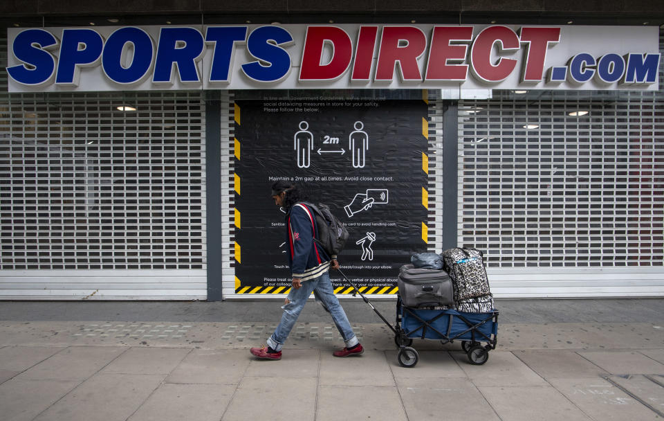 LONDON, UNITED KINGDOM - JUNE 12: A man pulls luggage past a social distancing sign on the door of Sports Direct on Oxford Street on June 12, 2020 in London, England.  As the British government further relaxes Covid-19 lockdown measures in England, this week sees preparations being made to open non-essential stores and Transport for London handing out face masks to commuters. International travelers arriving in the UK will face a 14-day quarantine period. (Photo by Justin Setterfield/Getty Images)
