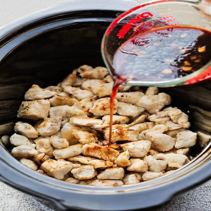 Pouring sweet and sour sauce over chicken in a slow cooker.