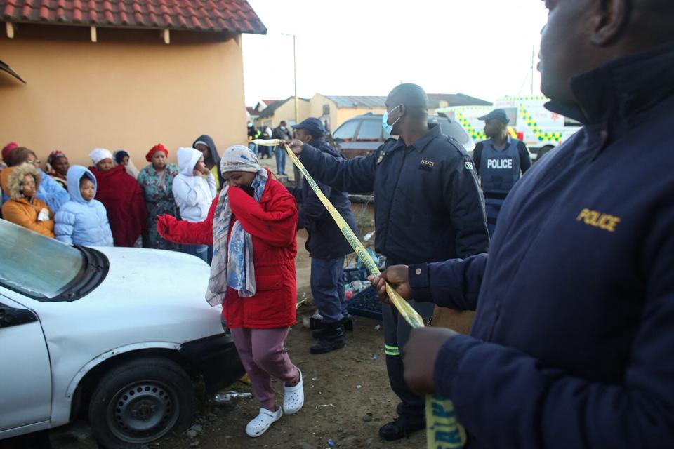 Members of the community and family wait for news outside a township pub in South Africa's southern city of East London on June 26, 2022, after 20 teenagers died. - At least 20 teenagers, the youngest aged just 13 years, have died at a township pub in South Africa's southern city of East London, but the cause of the deaths is still unclear. Crowds of people including parents whose children were missing gathered outside the tavern located along a street in a residential township as mortuary vehicles collected bodies, according to an AFP correspondent.