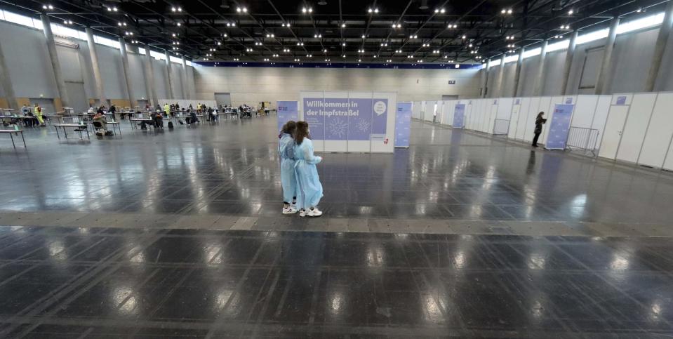 Medical workers walk in front of a poster that reads " Welcome to vaccination street!" walk through a vaccination center at the start mass vaccination in Vienna, Austria, Friday, Jan. 15, 2021. Authorities started to vaccinate the most vulnerable people in a coordinated effort. (AP Photo/Ronald Zak)